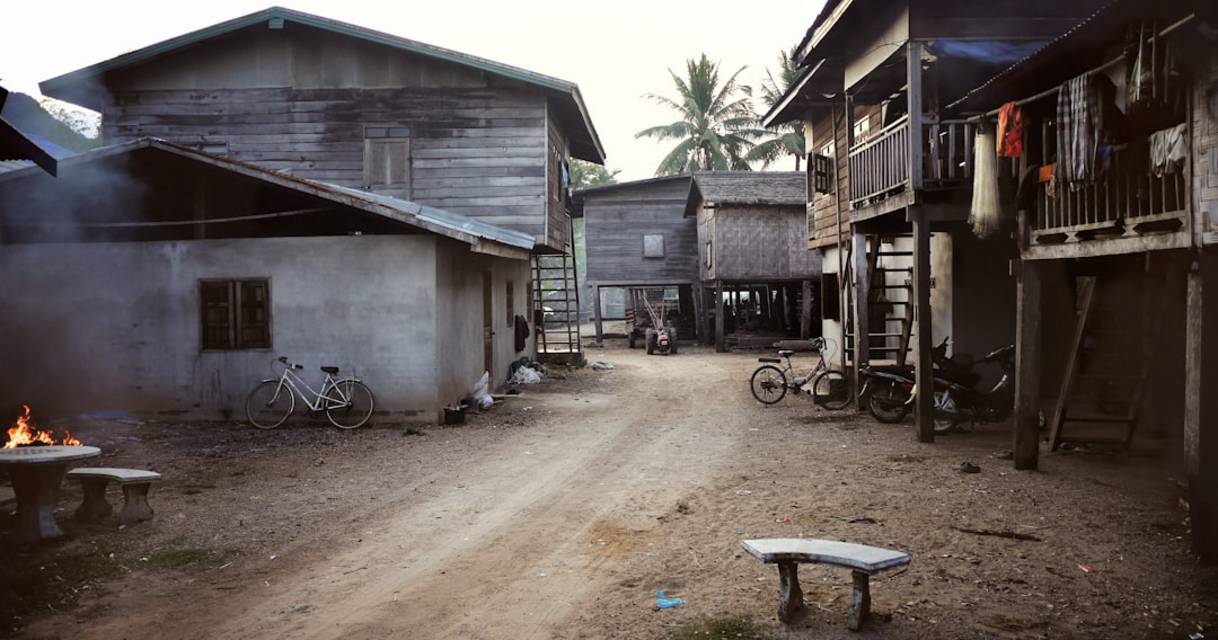 a dirt road in a village with buildings and bicycles WnK67bzcMHc